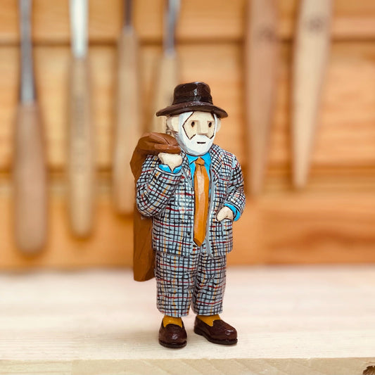 Personalized wooden figurine with a white beard, brown hat and checked suit, carrying a coat over one shoulder.