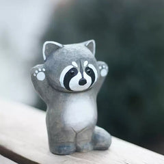 Raccoon figurine with both arms raised on wooden ledge