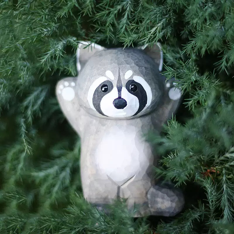 Raccoon figurine looking up through green foliage