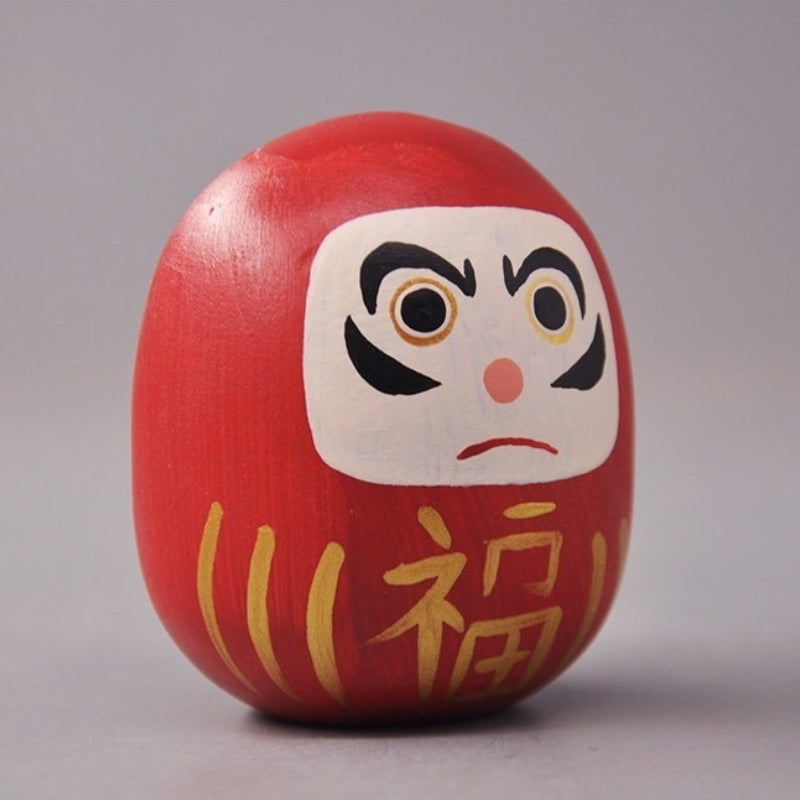 Side view of red daruma doll with painted facial details