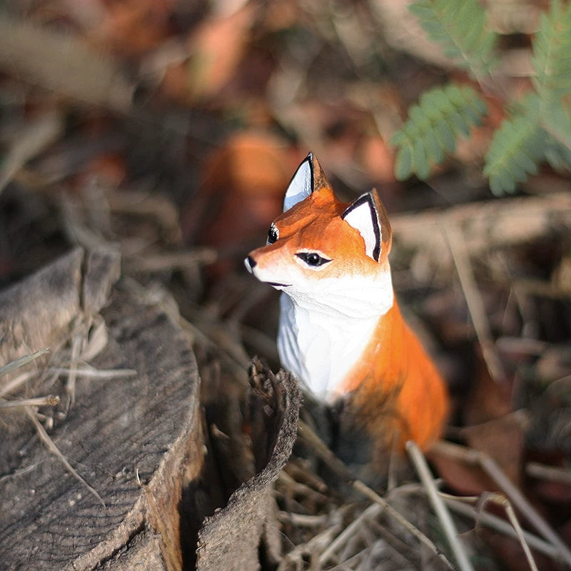 Sitting red fox figurine among autumn leaves