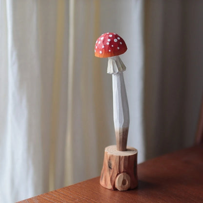 Red mushroom pen with a white-spotted cap standing in a carved wooden stump holder.