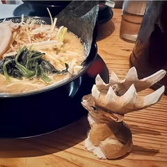 Reindeer figurines Christmas style – small antlered wooden reindeer placed beside ramen in cozy restaurant setting.
