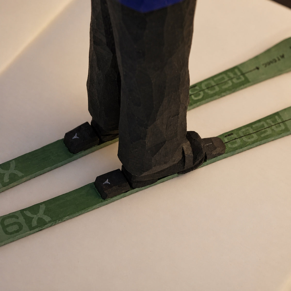 Carved black ski boots and bindings on a pair of green wooden skis