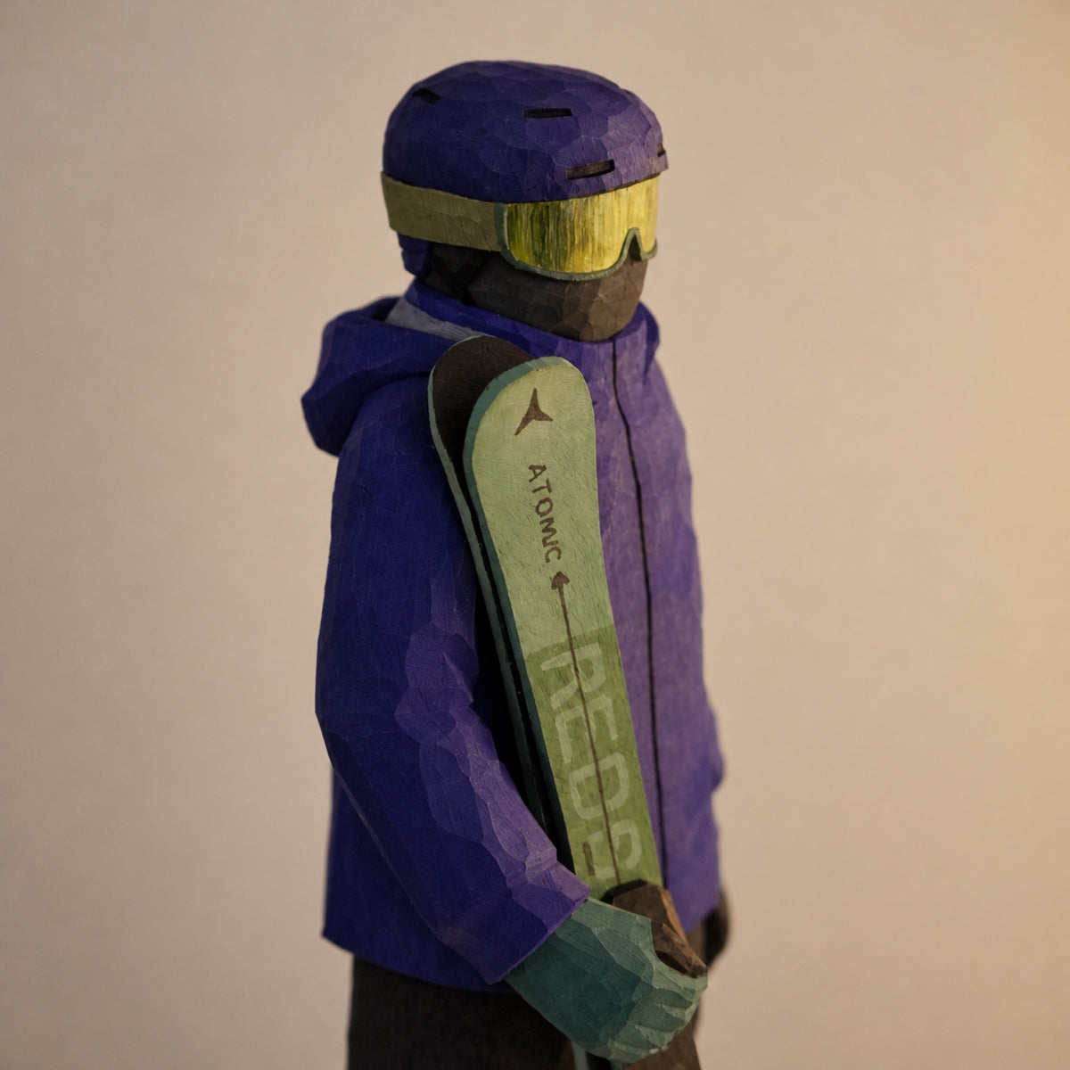 Close-up of a wooden skier's helmet, yellow goggles, green skis, and gloved hand