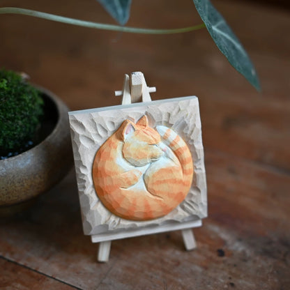 Sleeping cat wood carving on easel with plant