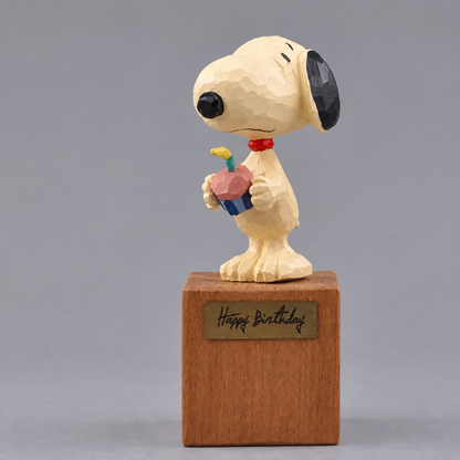 Snoopy birthday figurine holding a pink cupcake on a wooden Happy Birthday display block