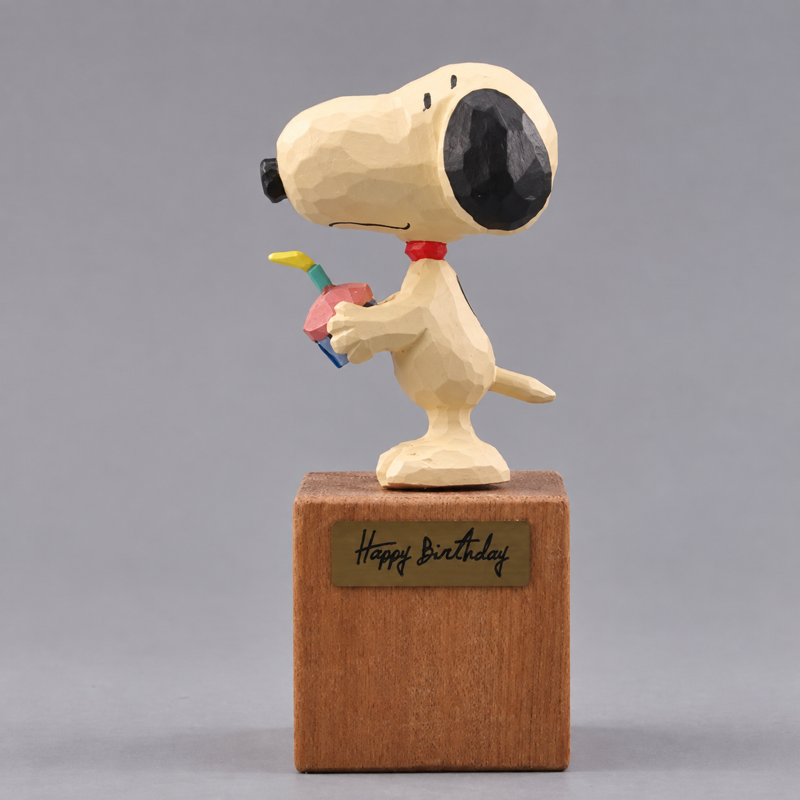 Side view of Snoopy holding the wooden cupcake, with black ear, red collar and tail visible