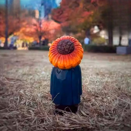Wooden sunflower man figure standing alone in a dry grassy field with autumn trees in the background.