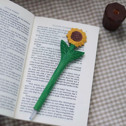 Wooden sunflower pen resting on an open book with its writing tip visible and brown pot holder nearby.