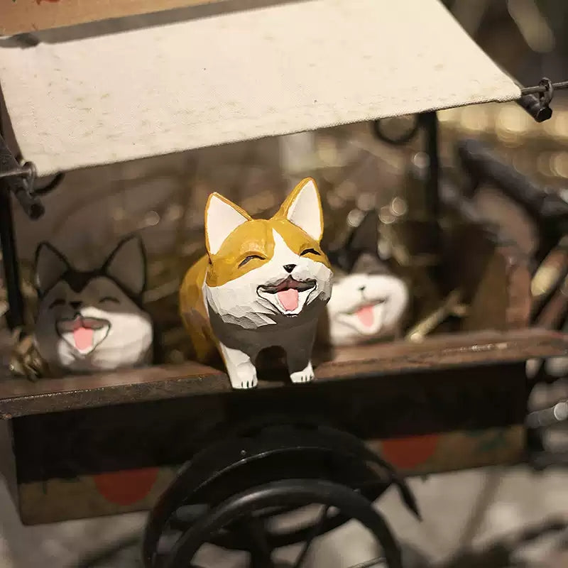Three laughing corgi figurines displayed in a miniature cart