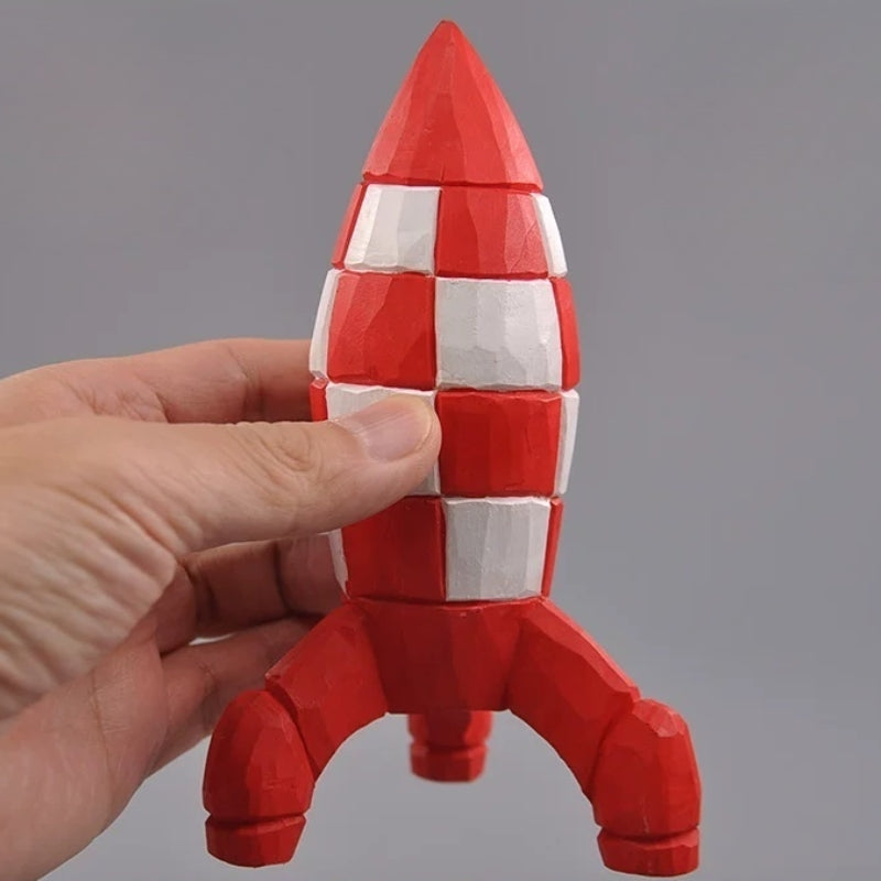 Hand-carved wooden Tintin rocket figurine held in one hand, showing its pointed nose and red-and-white checks