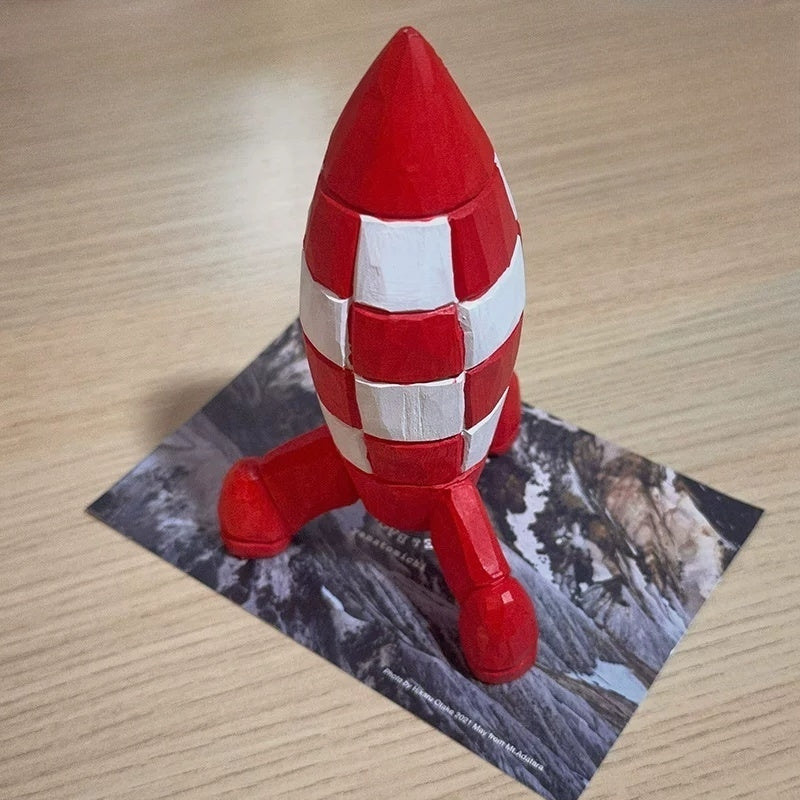 Wooden Tintin rocket viewed from above on a wooden tabletop with a printed landscape card beneath it