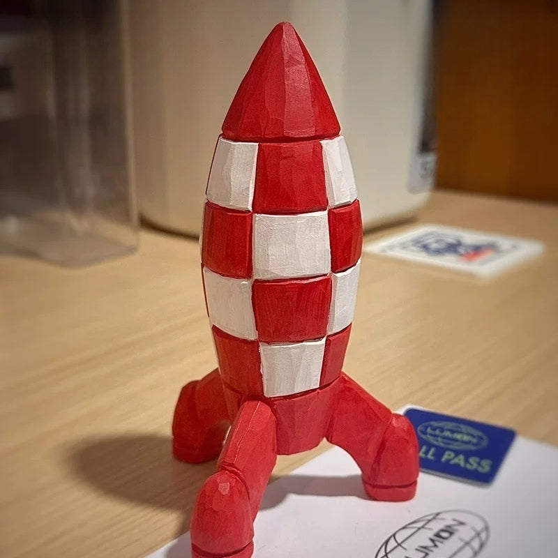 Three-quarter view of the red-and-white wooden Tintin rocket standing on a tabletop beside printed cards