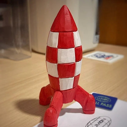 Three-quarter view of the red-and-white wooden Tintin rocket standing on a tabletop beside printed cards