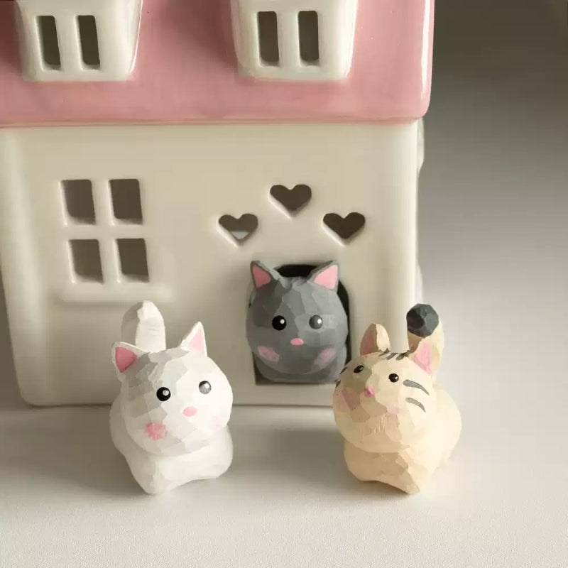 Three tiny cat figurines around ceramic house