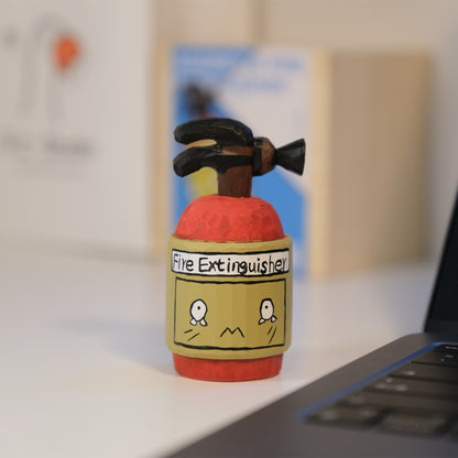 Hand-painted fire extinguisher figurine on desk next to laptop