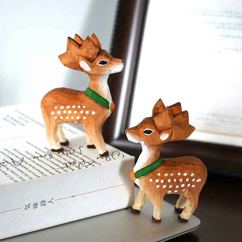 Two small Christmas deer figurines with green scarves displayed together beside books
