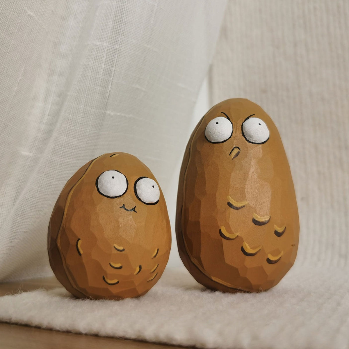 Two Wall-nut figurines displaying different emotions, placed against a white fabric backdrop.