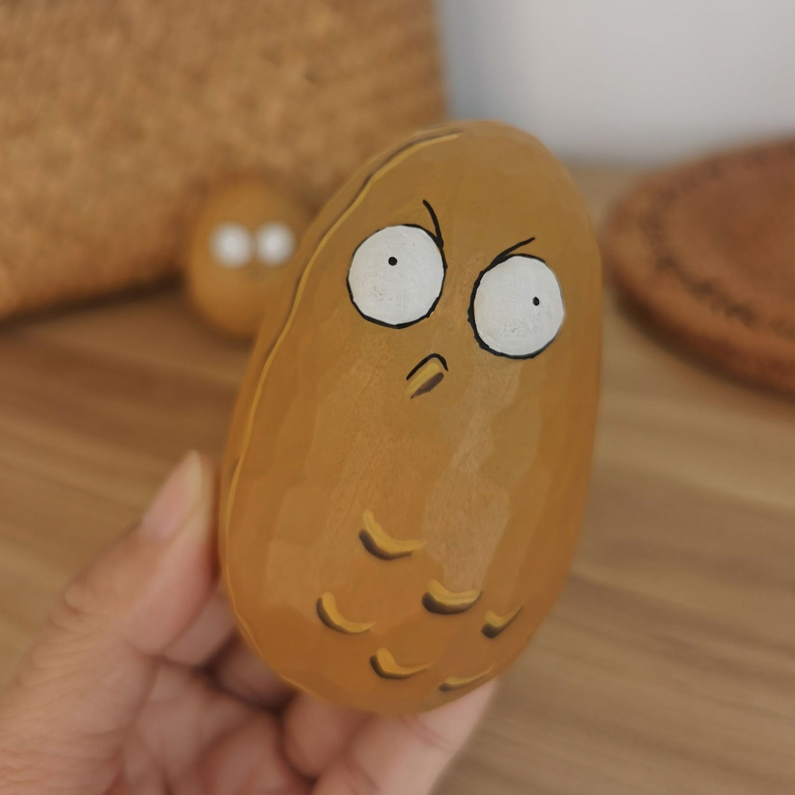 Hand holding a Wall-nut figurine showing a grumpy expression with another figurine in the background.