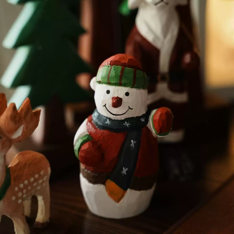 Waving snowman with a deer figure in the foreground and a Santa figure and wooden trees behind it