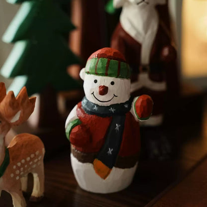 Waving snowman with a deer figure in the foreground and a Santa figure and wooden trees behind it