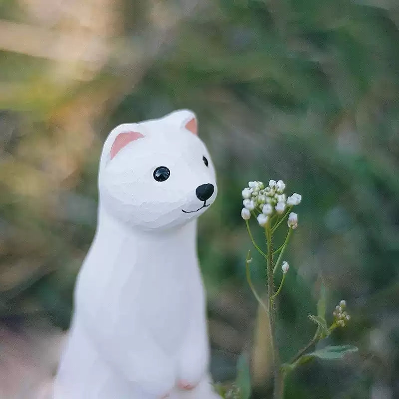 White weasel figurine facing small wildflowers