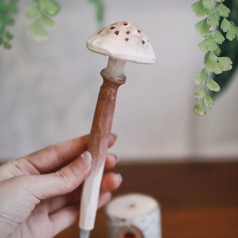 White-cap mushroom pen held in one hand, showing its carved brown and white stem and writing tip.