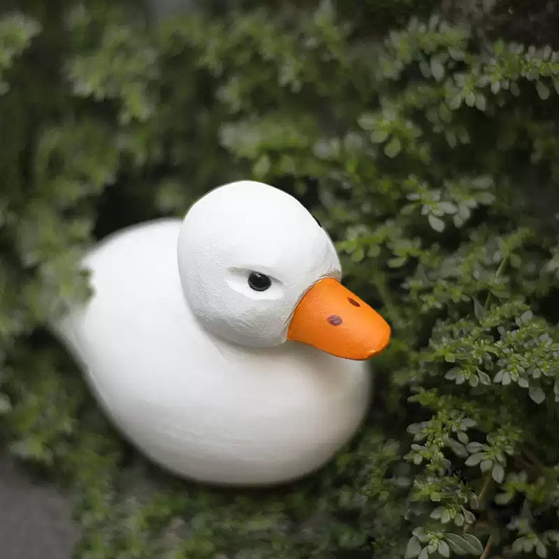 White duck figurine with round black eyes and a bright yellow-orange bill
