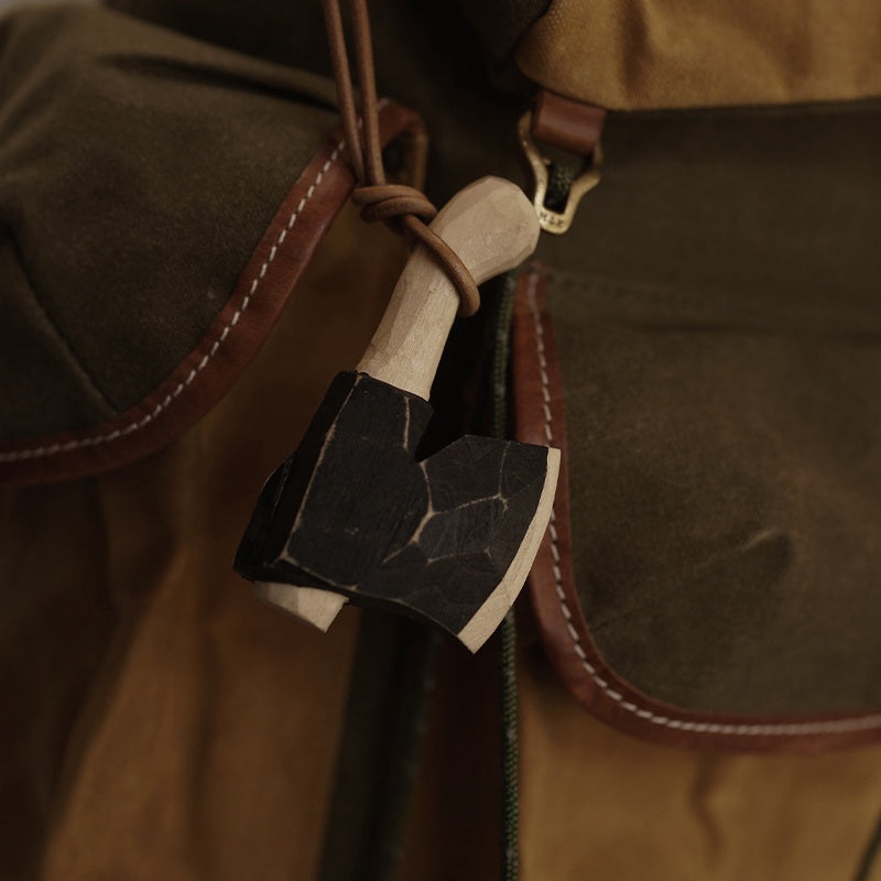 Wooden axe ornament hanging from a canvas backpack outdoors