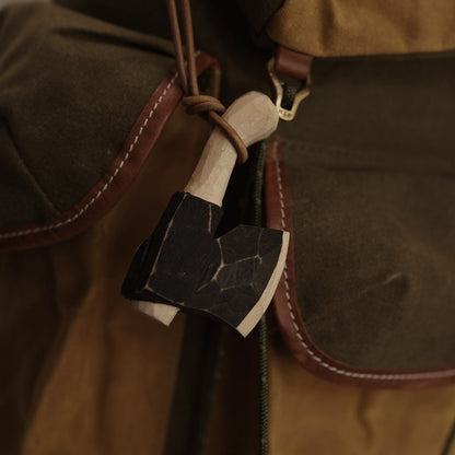 Wooden axe ornament hanging from a canvas backpack outdoors