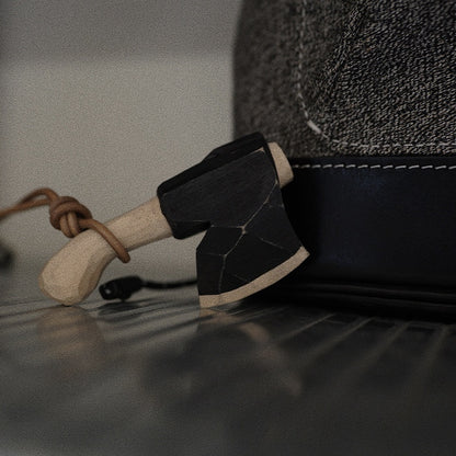 Hand-carved wooden axe ornament with leather cord beside a cap