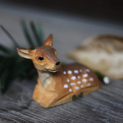 Resting baby wooden deer figurine with white spots and a faceted carved face