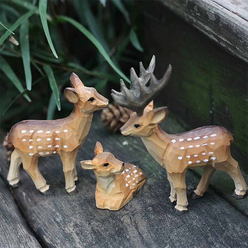 Three wooden deer figurines arranged as a family, with a resting fawn between two standing adults