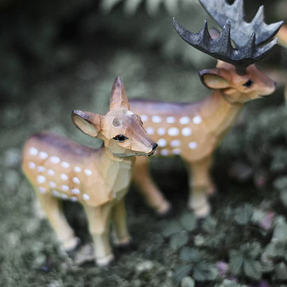 Two wooden deer figurines on moss, with the female in front and the antlered male behind