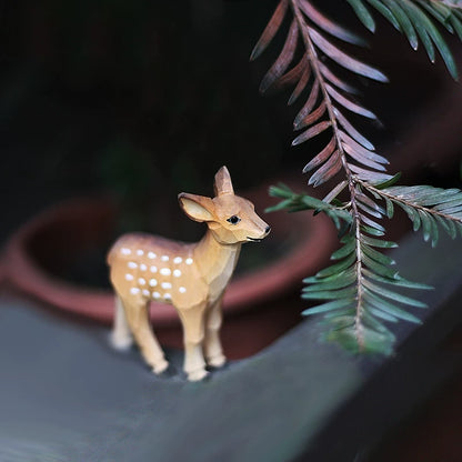 Standing female wooden deer figurine with white spots beside leafy branches