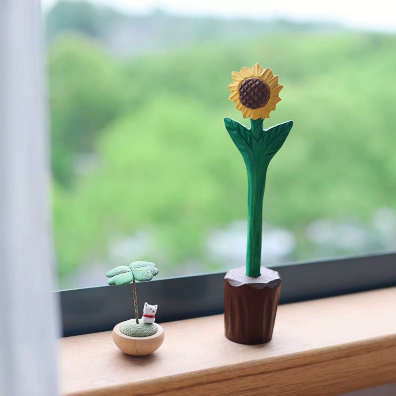 Wooden flower pen shaped like a sunflower in a brown pot holder beside a small clover and cat ornament.