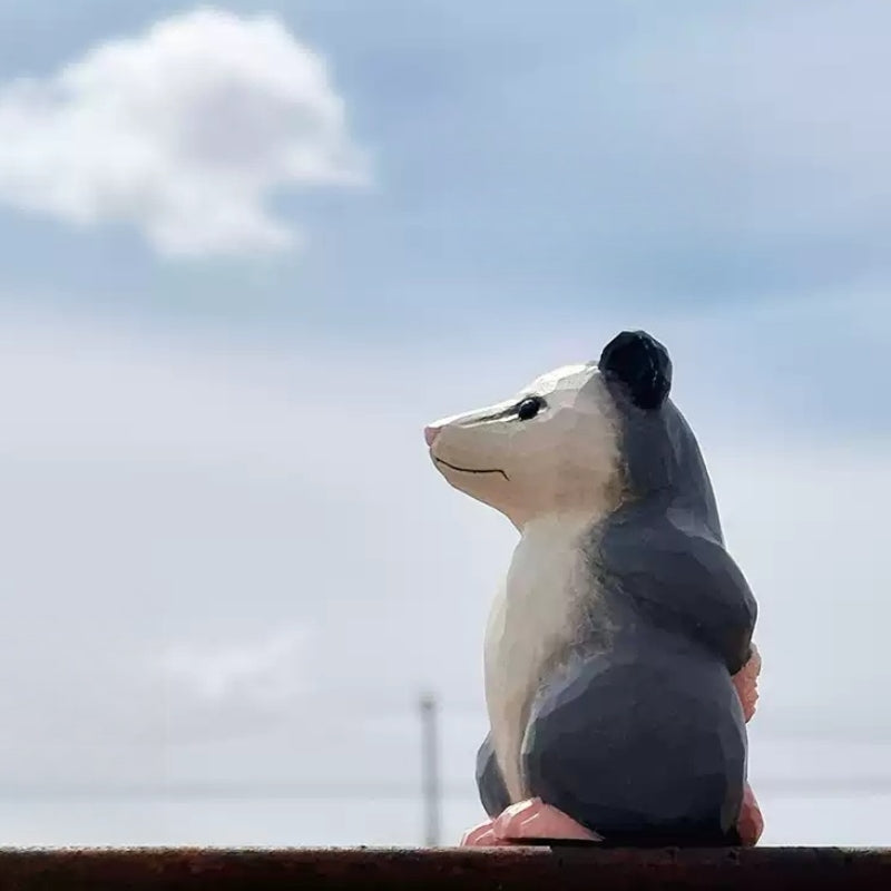 Wooden opossum figurine standing upright with a white face and pink feet