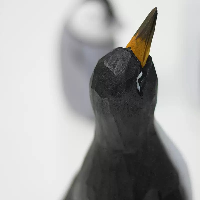 Close-up of a wooden penguin’s raised dark beak, yellow-orange base and curved white eye mark
