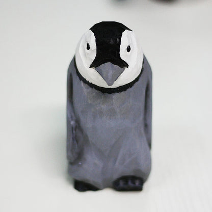 Gray wooden penguin chick with a white face, round black eyes and small dark feet, viewed from above