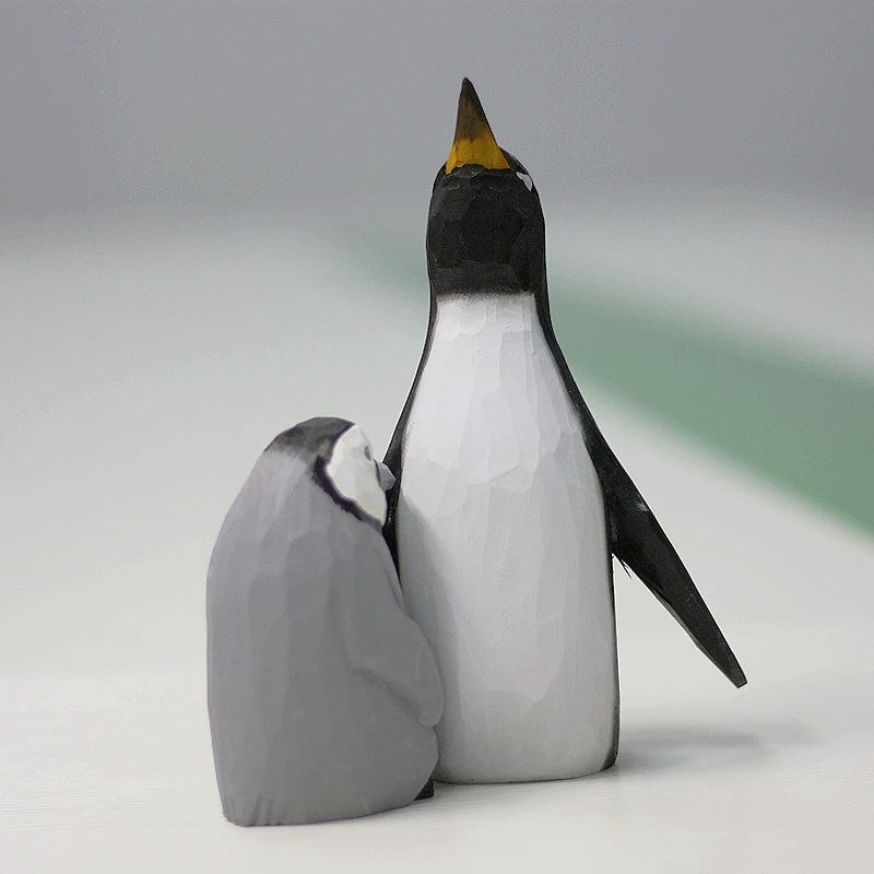 Wooden penguin figurines with the gray chick tucked beside the father’s white belly