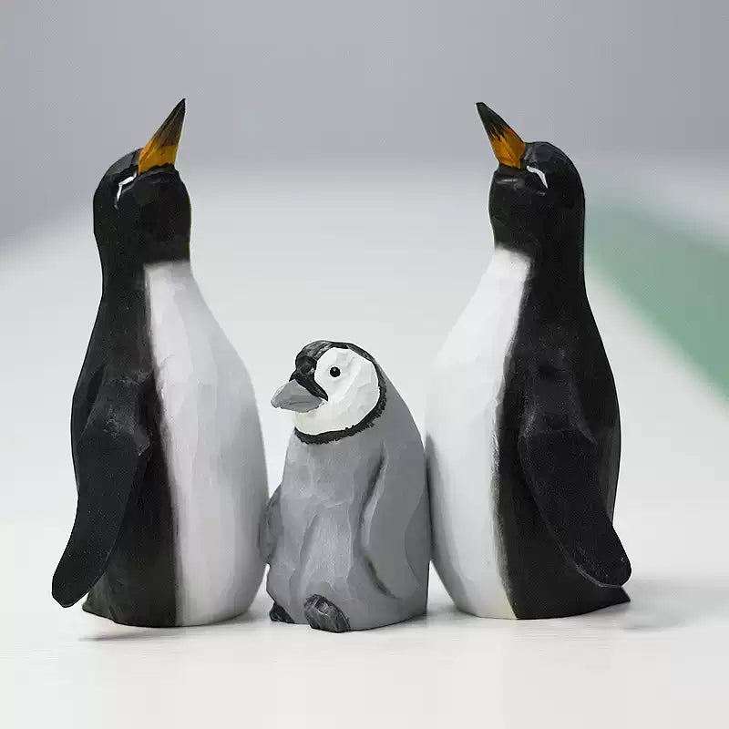 Three wooden penguins arranged together: two black-and-white adults and one gray chick