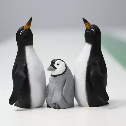 Three wooden penguins arranged together: two black-and-white adults and one gray chick