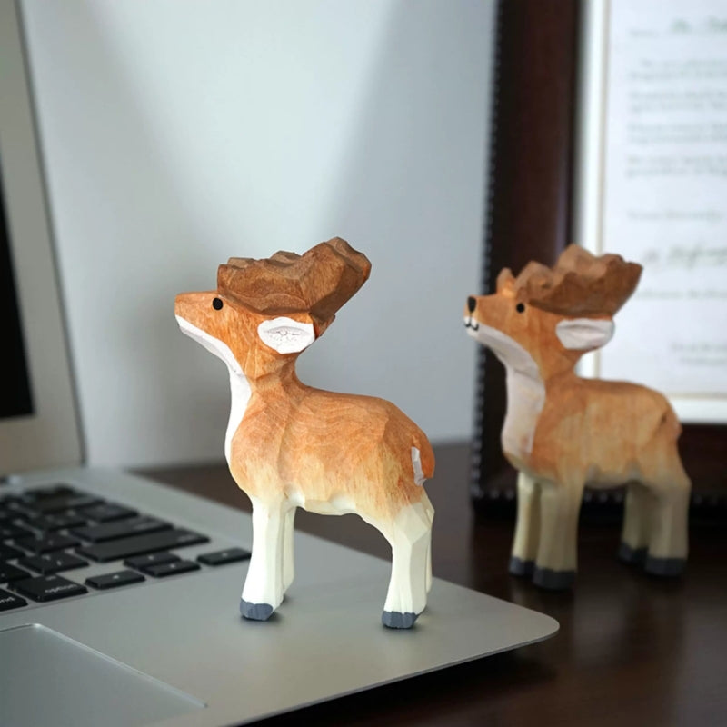 Two wooden reindeer figurines displayed beside a laptop and framed print
