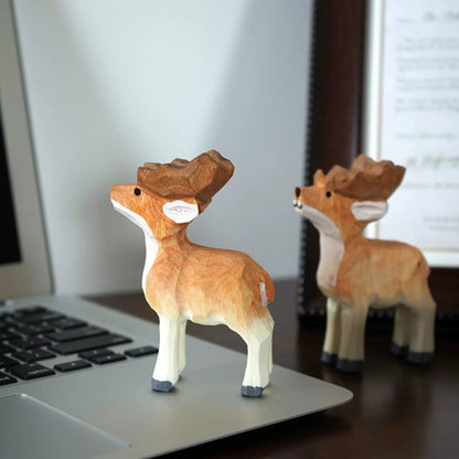 Two wooden reindeer figurines displayed beside a laptop and framed print