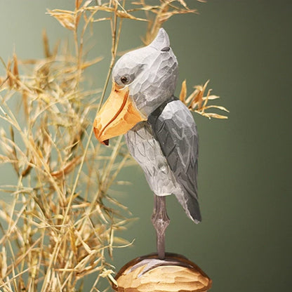 Wooden shoebill figurine in side profile with gray wings, long legs, and a large yellow bill
