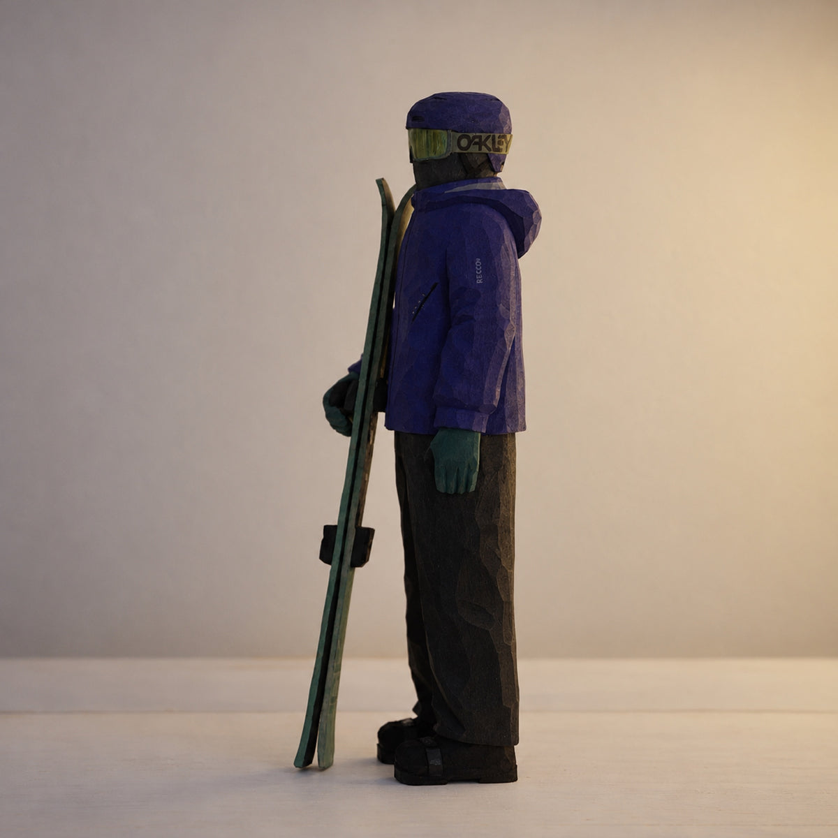 Side profile of a wooden skier holding skis, with a carved hood and green gloves