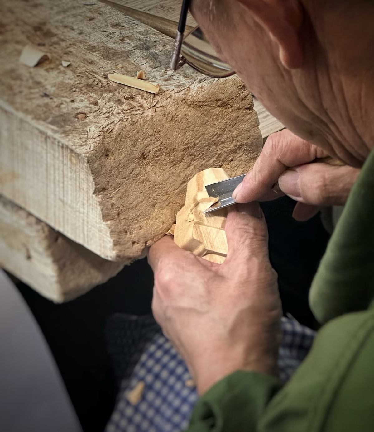 A carver leaning over the workbench to shape a small wooden figure