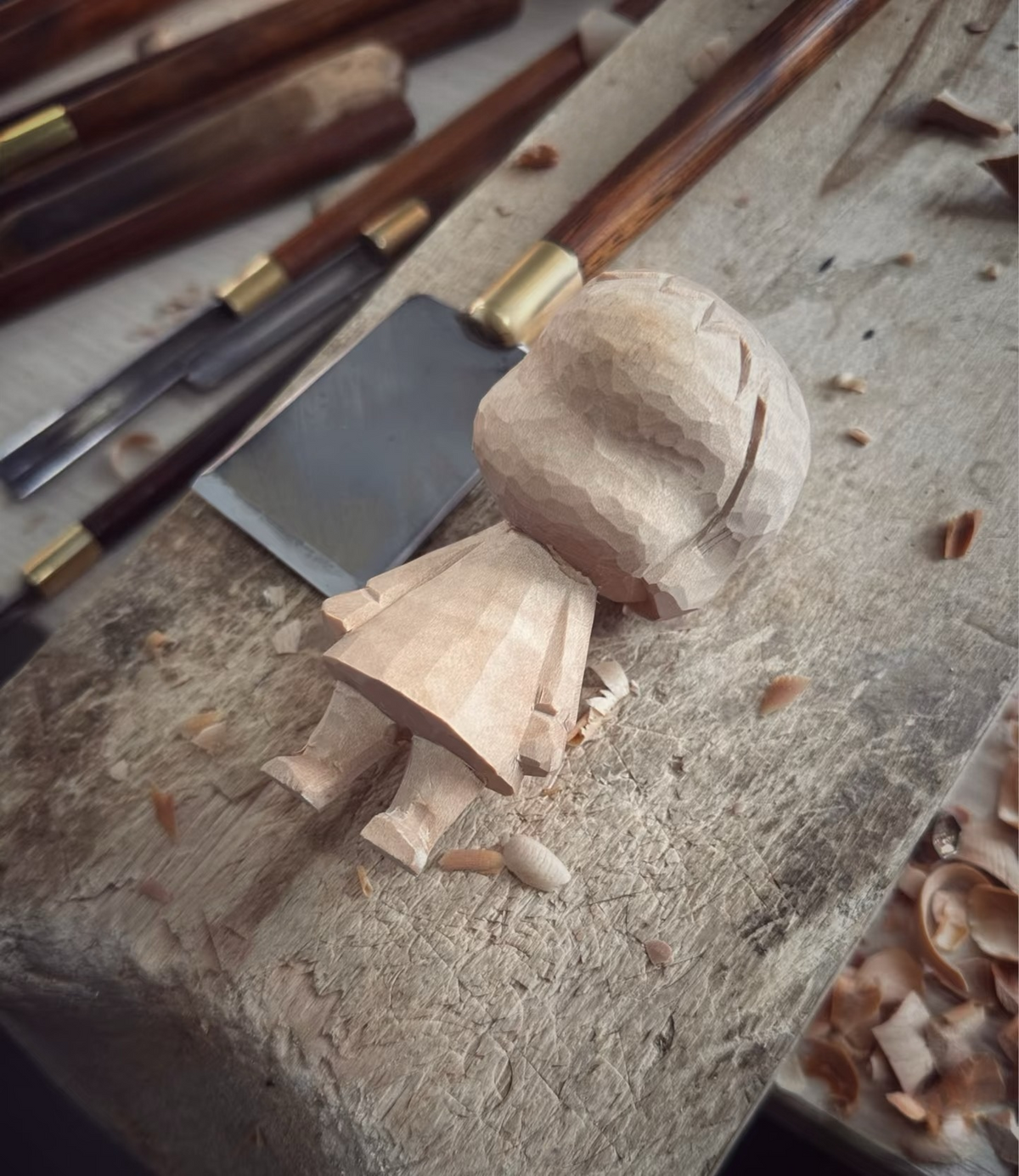 An unpainted wooden figure with a carved face and clothing beside hand tools