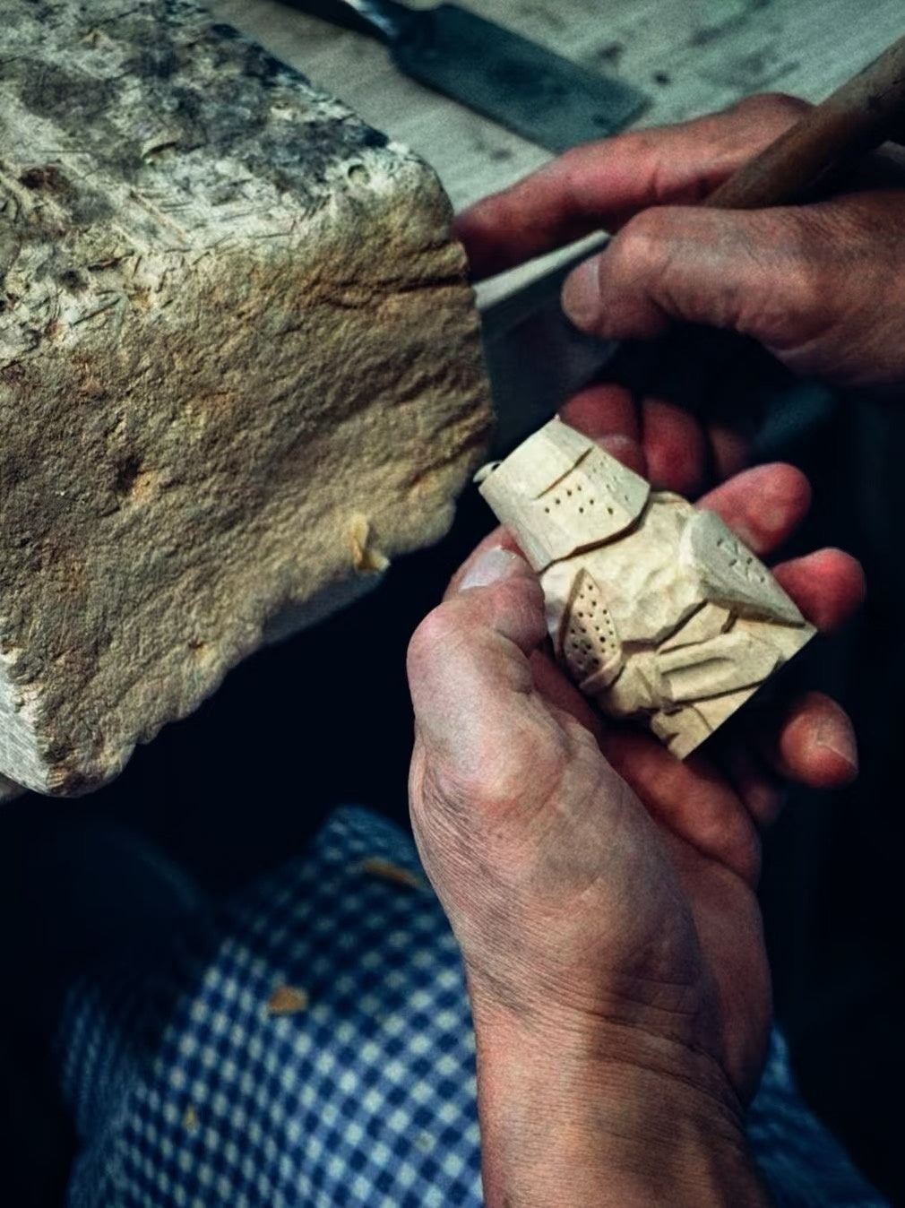 Hands shaping a small wooden figure at a workbench